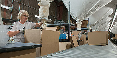 Worker packing products into cardboard boxes on a conveyor belt.