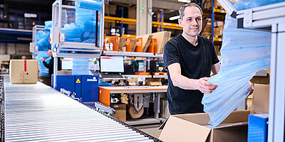 
									A man stands on a packing line and packs a box with bubble wrap.