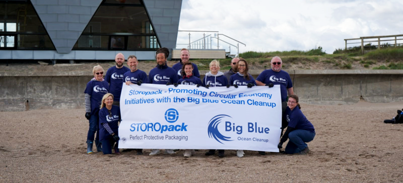 Storopack employees standing behind a banner for the organization Big Blue Ocean Cleanup on the beach