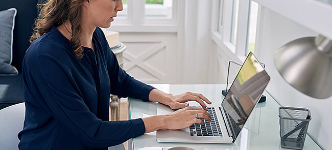 Woman working on a laptop at a home office desk.
