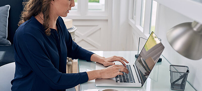 Woman working on a laptop at a home office desk.