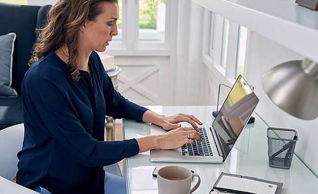 Woman working on a laptop at a home office desk.
