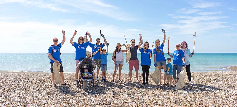 Am Strand sind mehrere Leute des Big Blue Ocean Cleanup Projekts  zu einem Gruppenfoto aufgestellt.