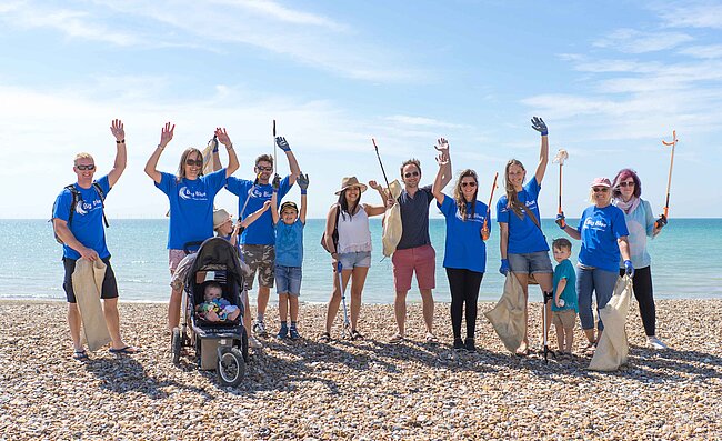 Am Strand sind mehrere Leute des Big Blue Ocean Cleanup Projekts  zu einem Gruppenfoto aufgestellt.