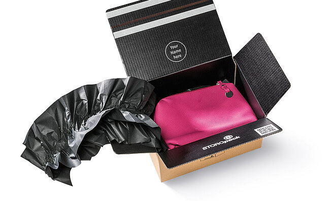 A cardboard box containing a pink bag and black paper cushions